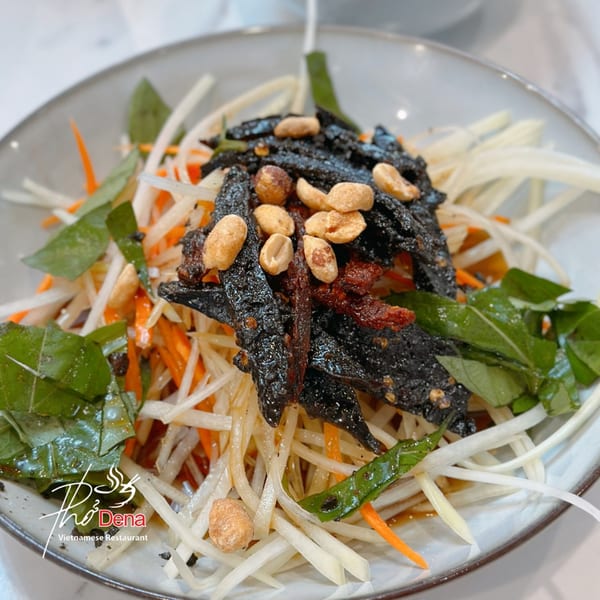 Vietnamese papaya salad with shredded papaya, carrots, dark crispy beef jerky, peanuts, and herbs.