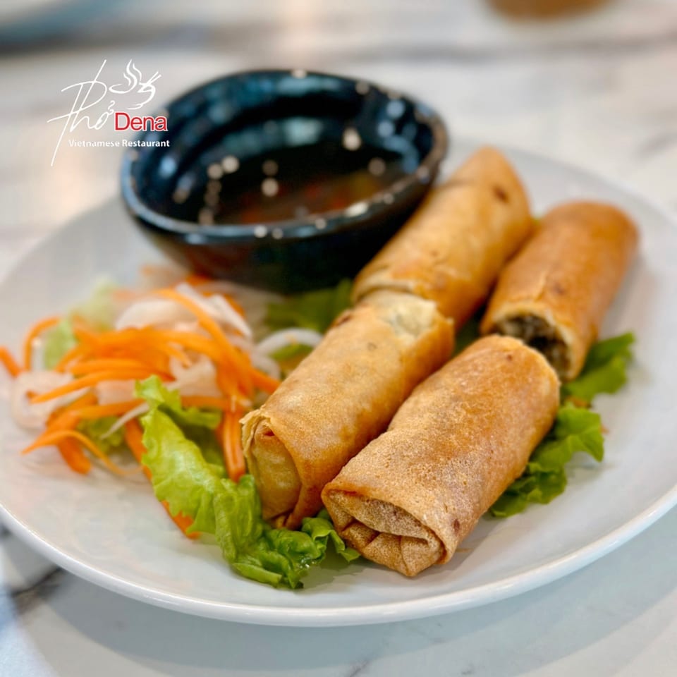 Three crispy Vietnamese spring rolls on a bed of lettuce and shredded carrots, with a dipping sauce.