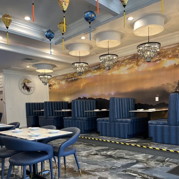 Interior of Pho Dena with blue booths, marble tables, chandeliers, and a mural of a sunset landscape.