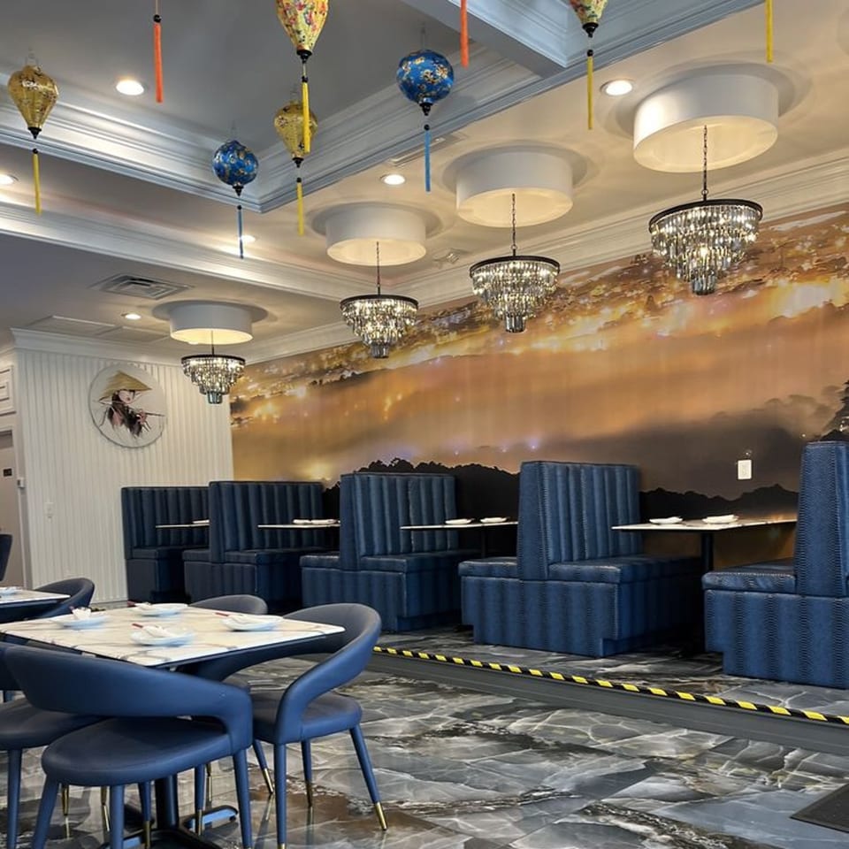 Interior of Pho Dena with blue booths, marble tables, chandeliers, and a mural of a sunset landscape.