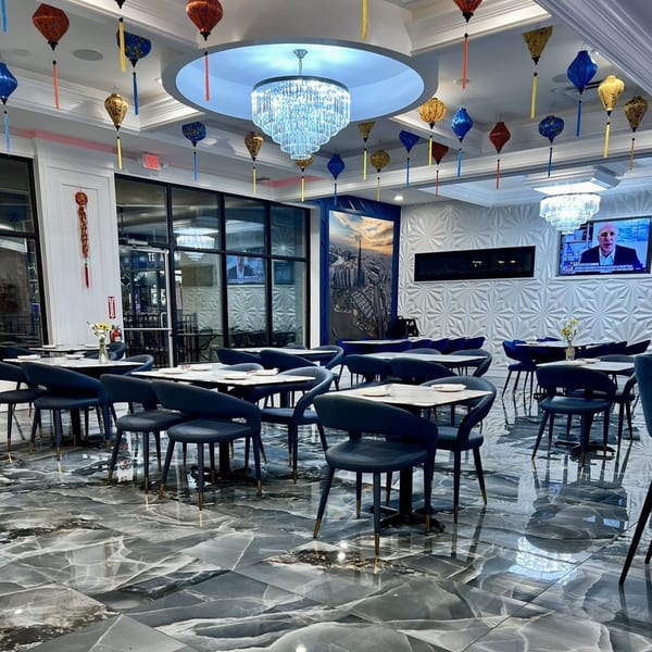 Interior of Pho Dena restaurant with blue chairs, marble tables, chandeliers, and colorful lanterns.