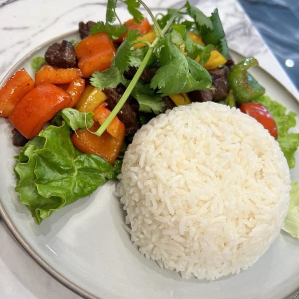 Shaking beef with bell peppers, onions, cilantro, and a side of white rice on a plate.