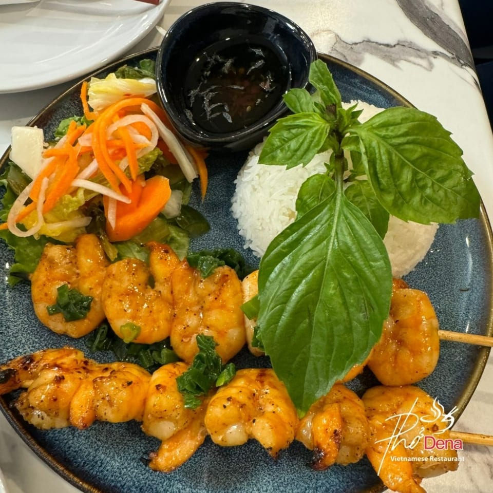 Grilled shrimp skewers with rice, salad, and a dipping sauce, garnished with fresh basil at Pho Dena.