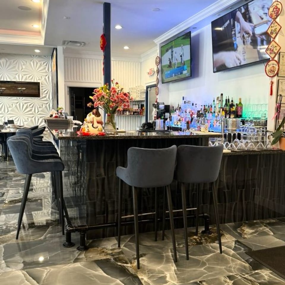 A sleek, modern bar with dark stools, a fully stocked liquor shelf, and two large TVs.