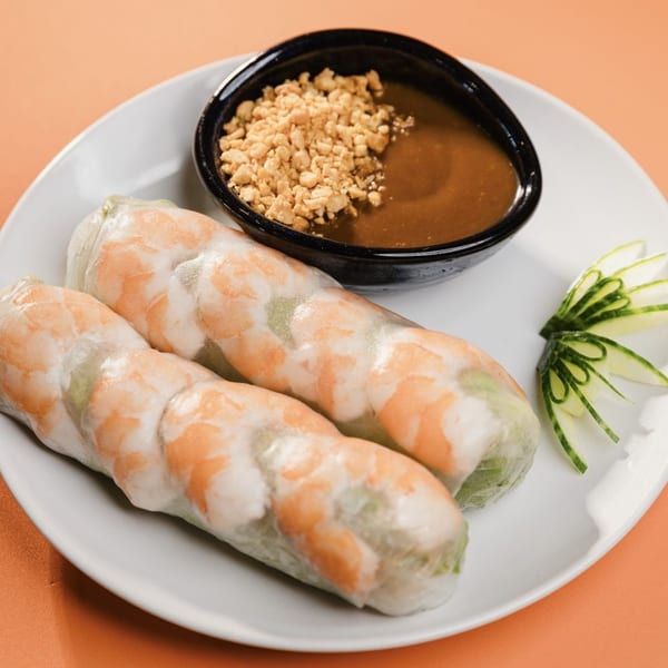 Two fresh Vietnamese spring rolls with shrimp, served with peanut sauce and cucumber garnish.