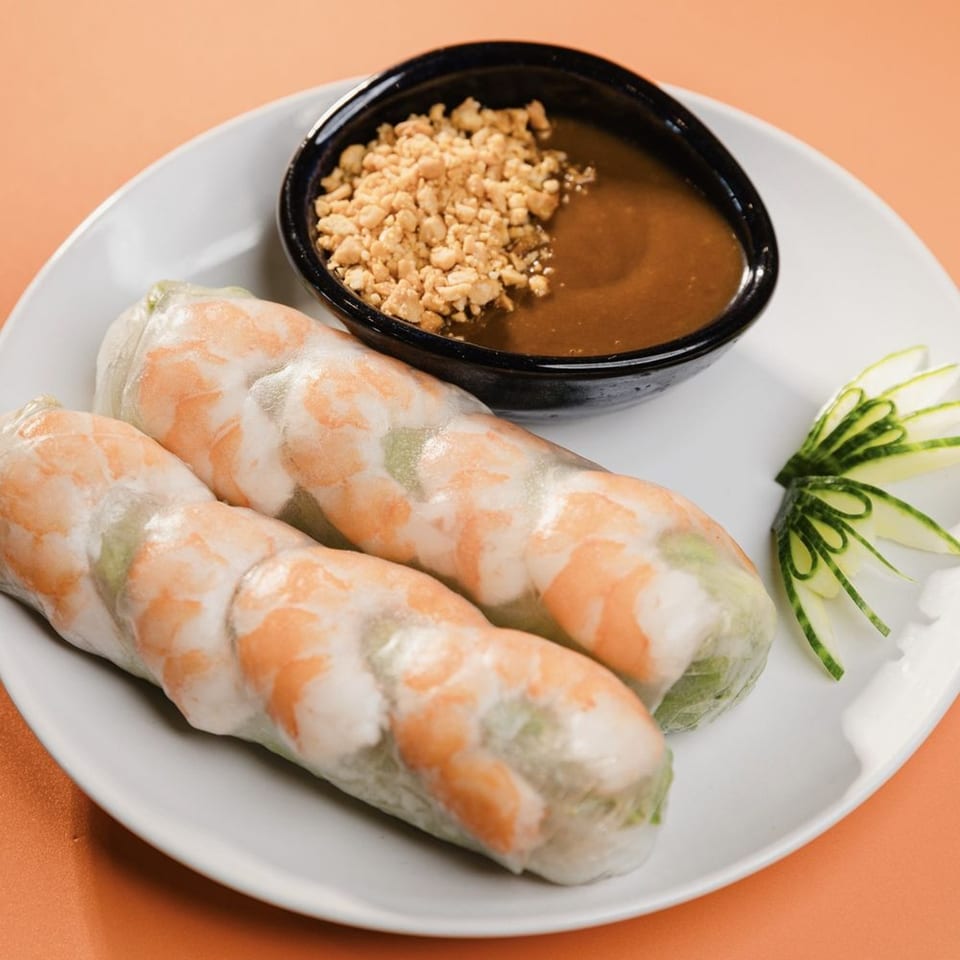 Two fresh Vietnamese spring rolls with shrimp, served with peanut sauce and cucumber garnish.
